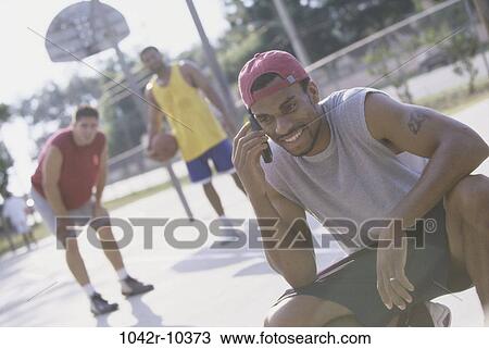 Young man talking on a mobile phone with two young men standing behind him View Large Photo Image Stock Image - Young man talking on a mobile phone with two young men standing behind him. Fotosearch