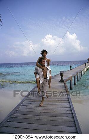 Young woman riding piggyback on a young man at a pier, Maldives View Large Photo Image Picture - Young woman riding piggyback on a young man at a pier, Maldives. Fotosearch