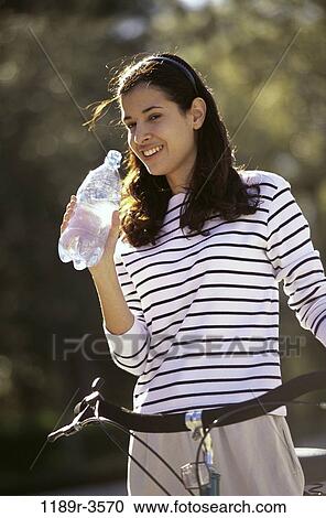Young woman standing with a bicycle holding a water bottle View Large Photo Image Stock Image - Young woman standing with a bicycle holding a water bottle. Fotosearch