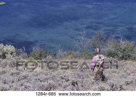 Stock Photography - Young woman walking down a hill holding a fishing rod, Idaho, USA. Fotosearch