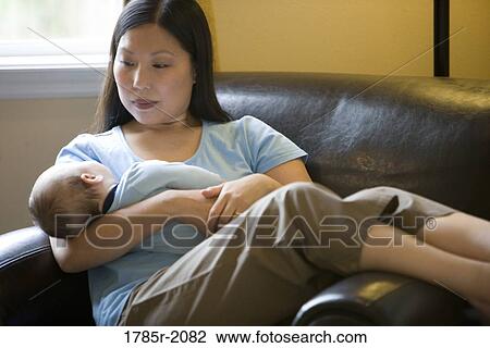 A mother lounges on a cozy chair holding a sleeping infant View Large Photo Image Stock Image - A mother lounges on a cozy chair holding a sleeping infant. Fotosearch