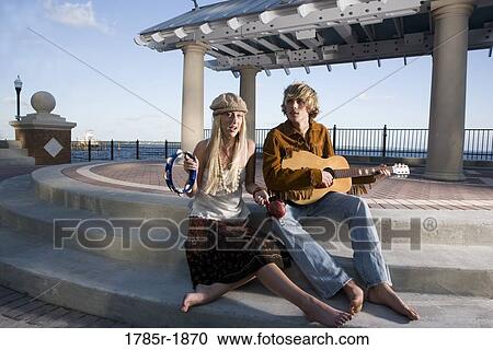 A young Hippie couple in a park playing guitar and tambourine View Large Photo Image Stock Image - A young Hippie couple in a park playing guitar and tambourine. Fotosearch