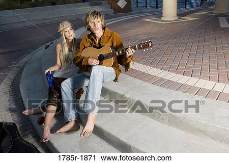 Stock Image - A young Hippie couple in a park playing guitar and tambourine. Fotosearch