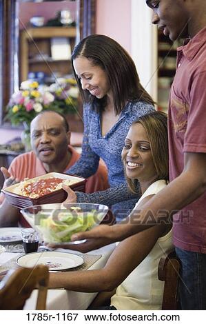 Stock Photo - Adult children serving food at family dinner. Fotosearch