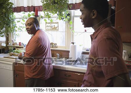 Stock Image - African American father and son talking in kitchen. Fotosearch