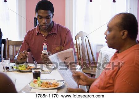 African American teenage boy using cellphone while father reads at dining table View Large Photo Image Stock Image - African American teenage boy using cellphone while father reads at dining table. Fotosearch