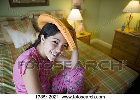 Asian-Caucasian teenage girl in pajamas sitting on her bed playing with a hat View Large Photo Image Stock Image - Asian-Caucasian teenage girl in pajamas sitting on her bed playing with a hat. Fotosearch