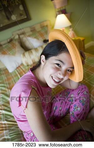 Asian-Caucasian teenage girl in pajamas sitting on her bed playing with a hat View Large Photo Image Stock Image - Asian-Caucasian teenage girl in pajamas sitting on her bed playing with a hat. Fotosearch