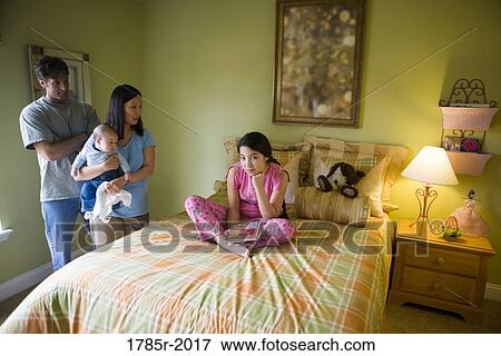 Asian-Caucasian teenage girl in pajamas sitting on her bed with parents standing over View Large Photo Image Stock Photo - Asian-Caucasian teenage girl in pajamas sitting on her bed with parents standing over. Fotosearch