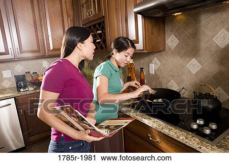 Asian mother and daughter cooking in wok holding cookbook View Large Photo Image Stock Image - Asian mother and daughter cooking in wok holding cookbook. Fotosearch