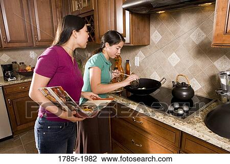 Asian mother and daughter cooking in wok holding cookbook View Large Photo Image Stock Image - Asian mother and daughter cooking in wok holding cookbook. Fotosearch