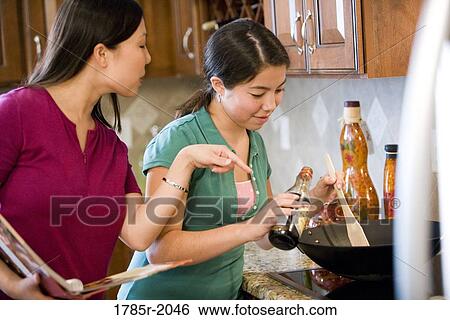 Asian mother daughter looking at cookbook and cooking in wok View Large Photo Image Stock Photograph - Asian mother daughter looking at cookbook and cooking in wok. Fotosearch