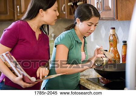 Asian mother daughter looking at cookbook and cooking in wok View Large Photo Image Stock Photography - Asian mother daughter looking at cookbook and cooking in wok. Fotosearch