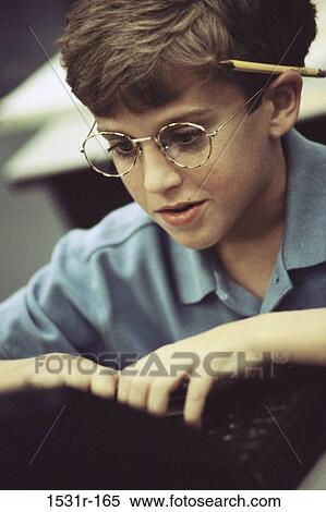 Stock Photography - Boy operating a laptop with a pencil behind his ear. Fotosearch