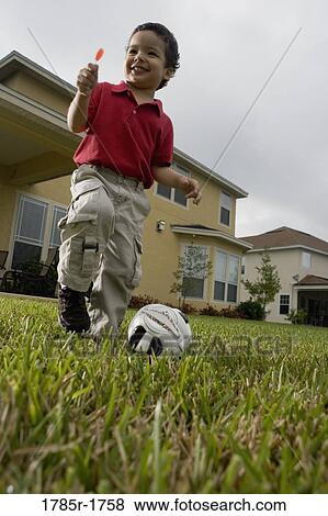 Stock Photo - Boy playing soccer while holding lollipop. Fotosearch