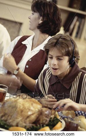 Boy sitting at a dining table wearing headphones View Large Photo Image Picture - Boy sitting at a dining table wearing headphones. Fotosearch