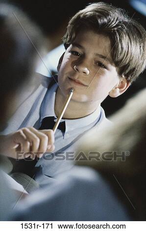 Boy sitting in a classroom with a pencil against his chin View Large Photo Image Stock Image - Boy sitting in a classroom with a pencil against his chin. Fotosearch