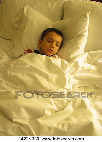 Stock Image - Boy sleeping in large bed. Fotosearch