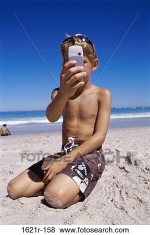 Stock Photo - Boy taking a photograph from a mobile phone on the beach. Fotosearch