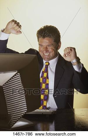 Businessman sitting in front of a computer with his hands raised View Large Photo Image Stock Photograph - Businessman sitting in front of a computer with his hands raised. Fotosearch