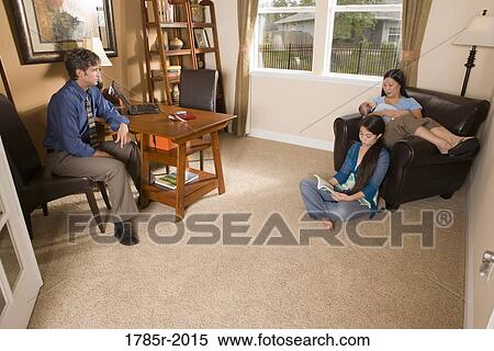 Stock Photography - Businessman using laptop computer in the study of his home while conversing with his family. Fotosearch