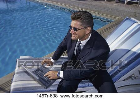 Stock Photo - Businessman with a laptop sitting near a swimming pool. Fotosearch