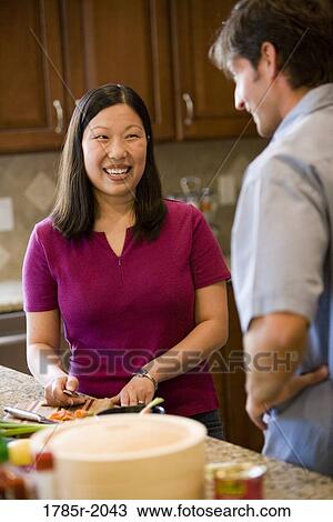 Caucasian man conversing with Asian woman while she prepares food in the kitchen View Large Photo Image Stock Image - Caucasian man conversing with Asian woman while she prepares food in the kitchen. Fotosearch
