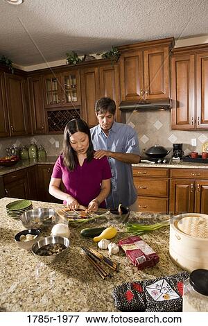 Caucasian man rubbing the shoulders of his Asian wife while she prepares food in the kitchen View Large Photo Image Stock Photo - Caucasian man rubbing the shoulders of his Asian wife while she prepares food in the kitchen. Fotosearch