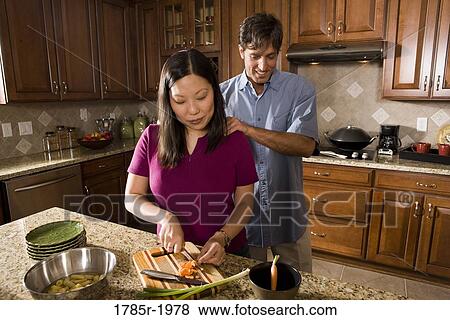 Caucasian man rubbing the shoulders of his Asian wife while she prepares food in the kitchen View Large Photo Image Stock Photo - Caucasian man rubbing the shoulders of his Asian wife while she prepares food in the kitchen. Fotosearch