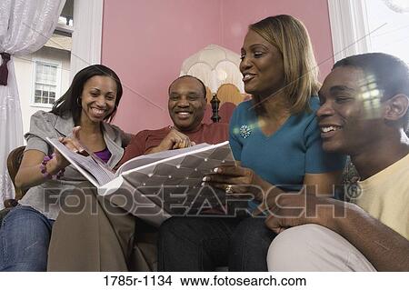 Cheerful family in living room looking at photo album View Large Photo Image Picture - Cheerful family in living room looking at photo album. Fotosearch