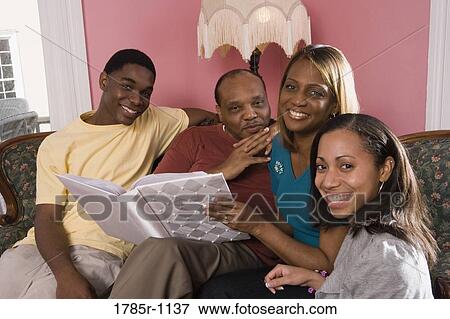 Cheerful family in living room looking at photo album View Large Photo Image Stock Photo - Cheerful family in living room looking at photo album. Fotosearch