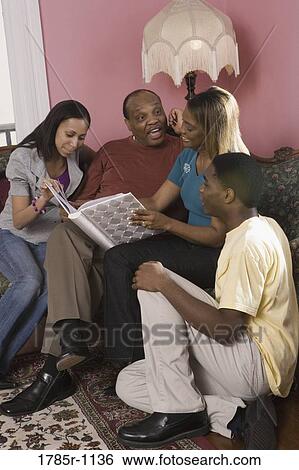Stock Photograph - Cheerful family in living room looking at photo album. Fotosearch