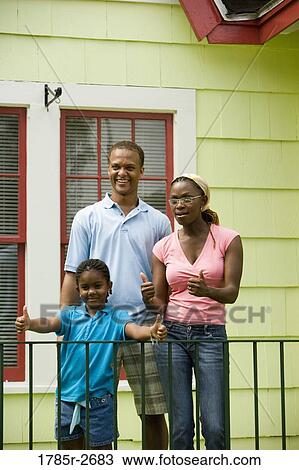 Cheerful family standing by a railing outside a house View Large Photo Image Stock Image - Cheerful family standing by a railing outside a house. Fotosearch