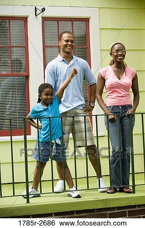 Cheerful family standing by a railing outside a house View Large Photo Image Stock Photograph - Cheerful family standing by a railing outside a house. Fotosearch