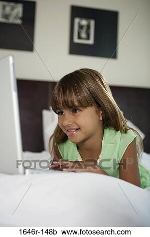 Stock Image - Close-up of a girl lying in the bed and using a laptop. Fotosearch