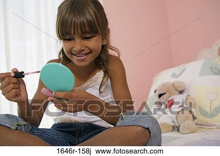 Stock Image - Close-up of a girl sitting in the bed and holding a hand mirror. Fotosearch