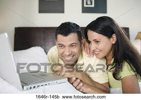 Stock Image - Close-up of a mature couple lying in front of a laptop and smiling. Fotosearch