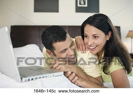 Close-up of a mature couple lying in front of a laptop and smiling View Large Photo Image Stock Image - Close-up of a mature couple lying in front of a laptop and smiling. Fotosearch