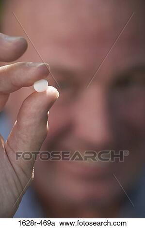 Stock Image - Close-up of a mature man showing a pill. Fotosearch