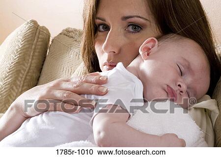Stock Image - Close-up of a mother holding a sleeping infant on her shoulders. Fotosearch