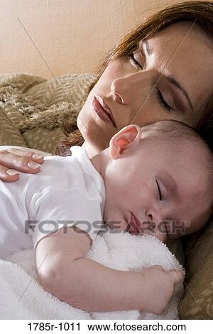 Stock Image - Close-up of a sleeping mother holding a sleeping infant on her shoulders. Fotosearch