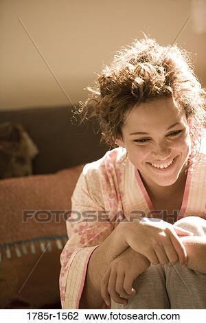 Close-up of a smiling young woman in a robe sitting on sofa View Large Photo Image Stock Image - Close-up of a smiling young woman in a robe sitting on sofa. Fotosearch