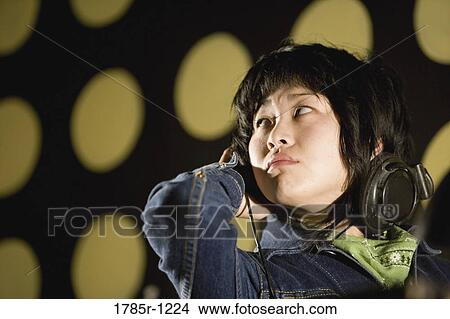Close-up of a young Asian woman listening to music on headphones looking away View Large Photo Image Picture - Close-up of a young Asian woman listening to music on headphones looking away. Fotosearch