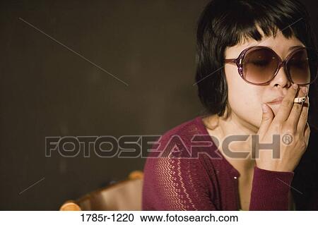 Stock Image - Close-up of a young Asian woman smoking a cigarette. Fotosearch