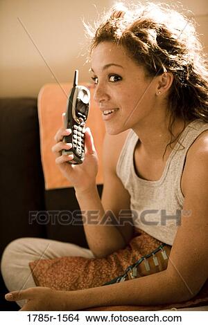 Close-up of a young woman sitting on sofa, talking on cordless phone View Large Photo Image Picture - Close-up of a young woman sitting on sofa, talking on cordless phone. Fotosearch