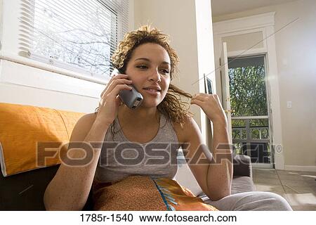 Stock Image - Close-up of a young woman sitting on sofa, talking on cordless phone. Fotosearch