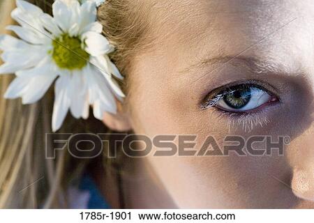 Close-up of a young woman's face, one eye and a flower in her hair visible View Large Photo Image Stock Image - Close-up of a young woman's face, one eye and a flower in her hair visible. Fotosearch