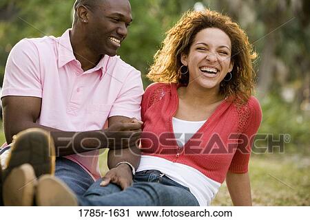 Stock Image - Close-up of amused young multi-ethnic couple sitting on grass outdoors. Fotosearch