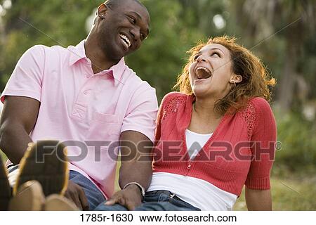 Close-up of laughing young multi-ethnic couple sitting on grass outdoors View Large Photo Image Stock Image - Close-up of laughing young multi-ethnic couple sitting on grass outdoors. Fotosearch
