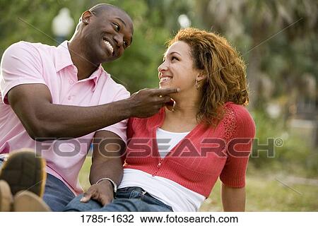 Close-up of smiling young multi-ethnic couple sitting on grass outdoors View Large Photo Image Stock Image - Close-up of smiling young multi-ethnic couple sitting on grass outdoors. Fotosearch